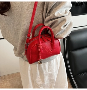Close-up of red lychee texture leather boston bag with silver bell pendant detail