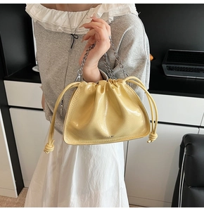 Detail of yellow glossy bucket bag with silver chunky chain handle and drawstring closure