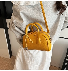 Detailed view of bright yellow leather bowling bag with silver hardware and woven charm