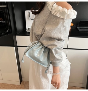 Close-up of light blue glossy drawstring bucket bag with silver metal chain strap detail