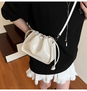 Close-up of white patent leather drawstring bucket bag with silver metal hooks and shiny finish