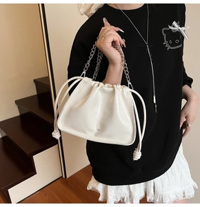 Detail of white pleated bucket bag with silver chain handle and drawstring closure