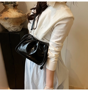 Detail shot of black glossy drawstring bucket bag with white brand logo and leather strap