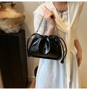 Detail of black glossy drawstring bucket bag with silver chain strap and logo
