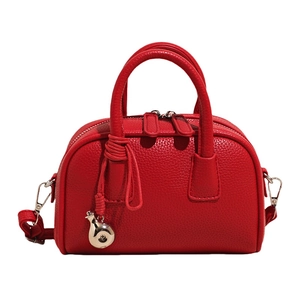 Red pebbled leather boston bag with dual handles and metal drop charm on white background