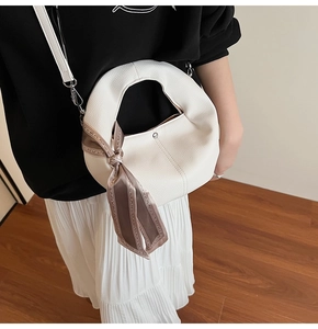Close-up of white crescent bag with lychee texture leather and decorative silk scarf