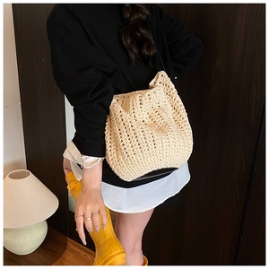 Detail of beige hollow-out woven straw tote bag worn over the shoulder by a model