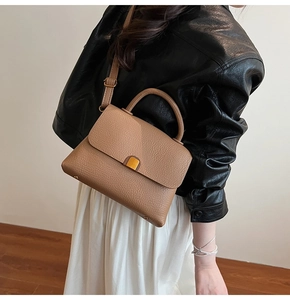 Sac à main en cuir grainé porté par un mannequin avec bandoulière et clous de fond