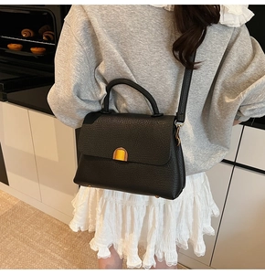 Close-up of black lychee grain leather handbag with gold magnetic closure and strap