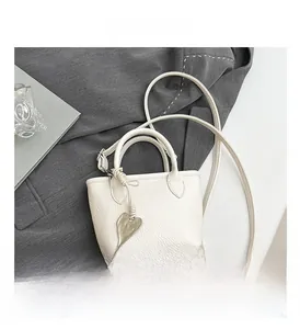 Macro shot of white pebble grain leather mini bucket bag with gold heart charm detail