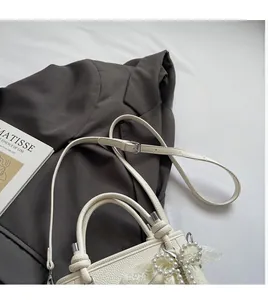 Détail du sac seau blanc crème texturé avec nœud en perles et bordure en dentelle