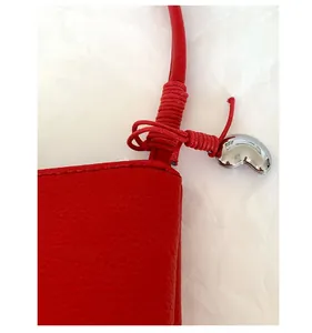 Détail d'un sac à bandoulière en cuir rouge à motif litchi avec pendentif cœur en argent