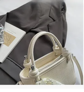 Détail du sac seau blanc à motif litchi avec poignée nouée et pendentif en perles