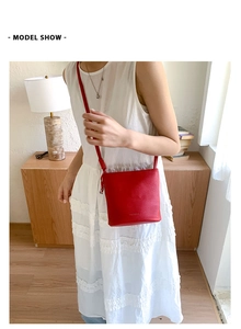 Détail d'un sac seau en cuir rouge avec une texture grainée et une bandoulière mince