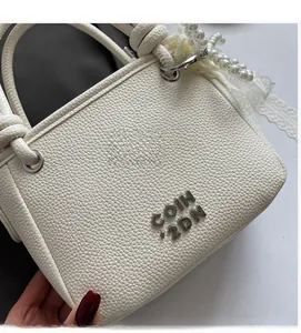 Gros plan du sac seau blanc en cuir grainé avec breloque en perles et logo en métal
