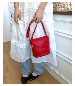 Détail du sac seau rouge en cuir grainé avec une décoration de boule argentée sur la sangle