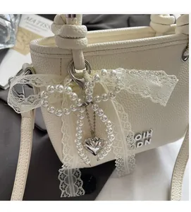 Détail du sac seau crème avec nœud en dentelle, chaîne en perles et pendentif cœur