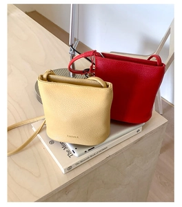 Vue détaillée de mini sacs seaux en cuir jaune et rouge sur une pile de livres blancs