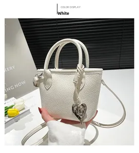 Close-up of white lychee leather square handbag with decorative silver heart pendant