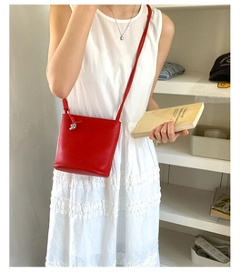 Sac seau rouge chic en cuir avec pendentif en métal porté à l'épaule sur une robe blanche