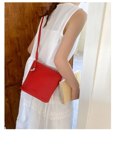 Détail du sac bandoulière en cuir rouge avec surface texturée et logo embossé élégant
