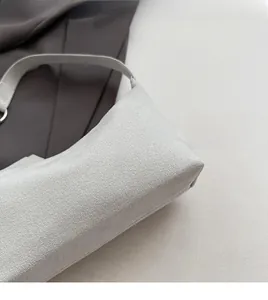 Detail shot of light grey suede texture and precise stitching on a minimalist handbag