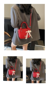 Détail du sac seau rouge à motif litchi avec nœud en dentelle et pendentif perle