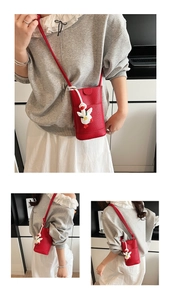 Detail of red litchi texture phone bag with cute white duck pendant and thin shoulder strap