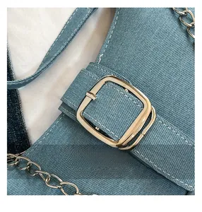 Detail of light blue denim crossbody bag with golden buckle and contrast stitching