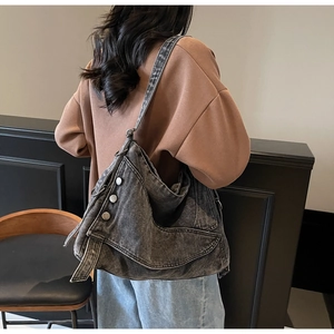 Detail of black washed denim tote bag featuring decorative metal buckles and topstitching