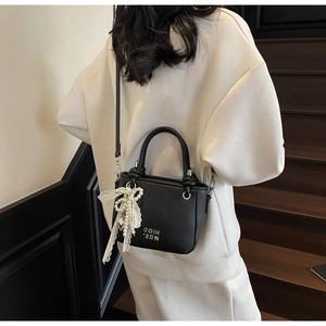 Close-up of black lychee grain leather bucket bag with lace pearl charm and long strap