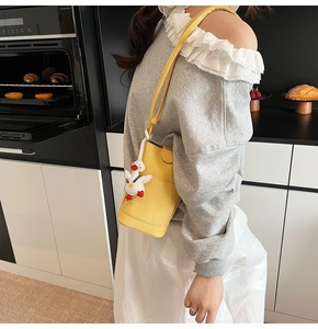 Detail of yellow pebbled leather bucket bag with cute duck charm and slim shoulder strap