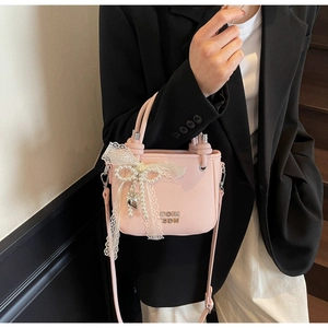 Détail du sac à main rose en cuir avec nœud en dentelle et perle sur un costume noir