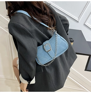 Detail of light blue denim shoulder bag featuring a large silver square buckle and chain