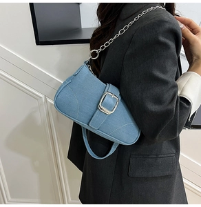 Detailed view of blue denim saddle bag featuring a polished silver square buckle and chain strap