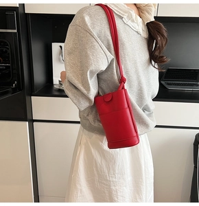 Detail of red cylinder crossbody bag showing premium pebbled leather texture and shoulder strap
