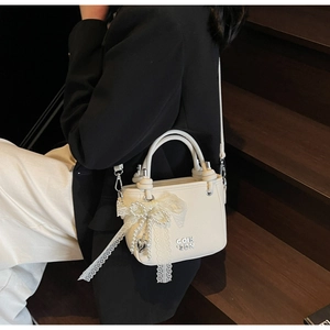 Détail du sac blanc cassé texture lychee avec nœud en dentelle, perles et pendentif cœur