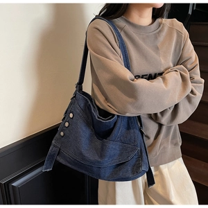 Detail of dark blue denim hobo bag featuring silver metal rivets and frayed edge straps