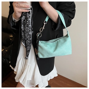 Detail of mint green suede shoulder bag with silver chain strap on black blazer outfit