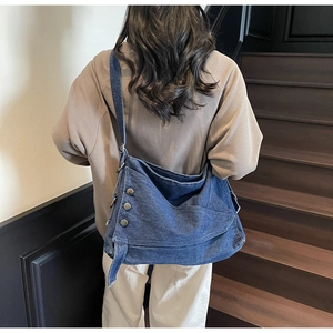 Detail of dark blue denim tote bag with silver studs and wide strap on model