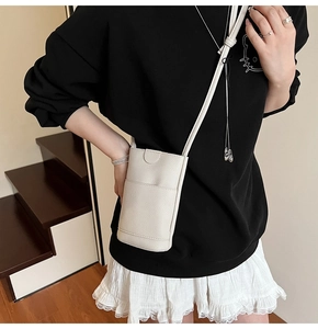 Détail d'un mini sac bandoulière en cuir grainé beige avec poche frontale sur modèle