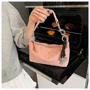 Pink suede hobo bag with silver heart charm and rope knot strap detail shown by hand
