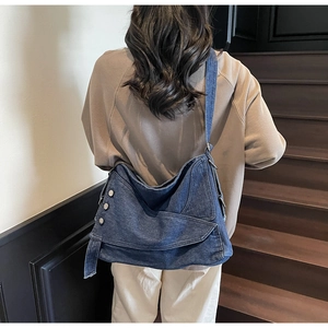 Detail of a blue denim tote bag with frayed edges and silver metal buckle on a shoulder strap