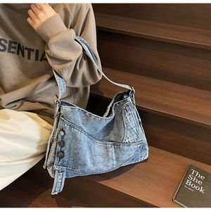 Close-up of vintage blue denim shoulder bag with decorative metal buttons on dark wood stairs