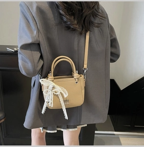 Detail of beige litchi grain bucket bag with large lace bow and pearl pendant