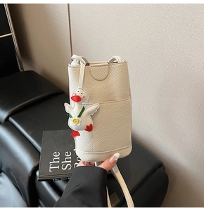 Detail of creamy white pebble leather phone bag with a cute duck charm and slim strap