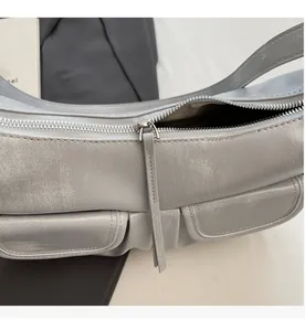 Detail of silver metallic shoulder bag showing smooth zipper and front flap pockets