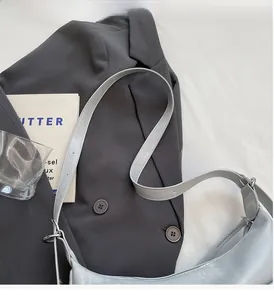Detail of silver metallic crescent bag with adjustable strap on a grey blazer backdrop