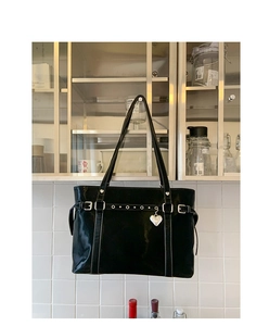 Detail of black glossy tote bag featuring silver heart charm and belted strap buckles