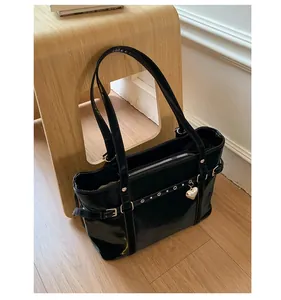 Detail of glossy black patent leather tote bag with silver heart pendant and stud details